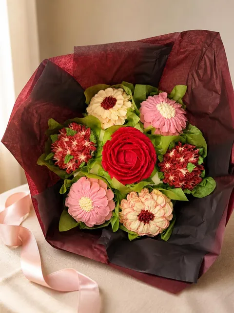 A bouquet of seven cupcakes piped as pink, cream and red buttercream flowers, wrapped in tissue paper