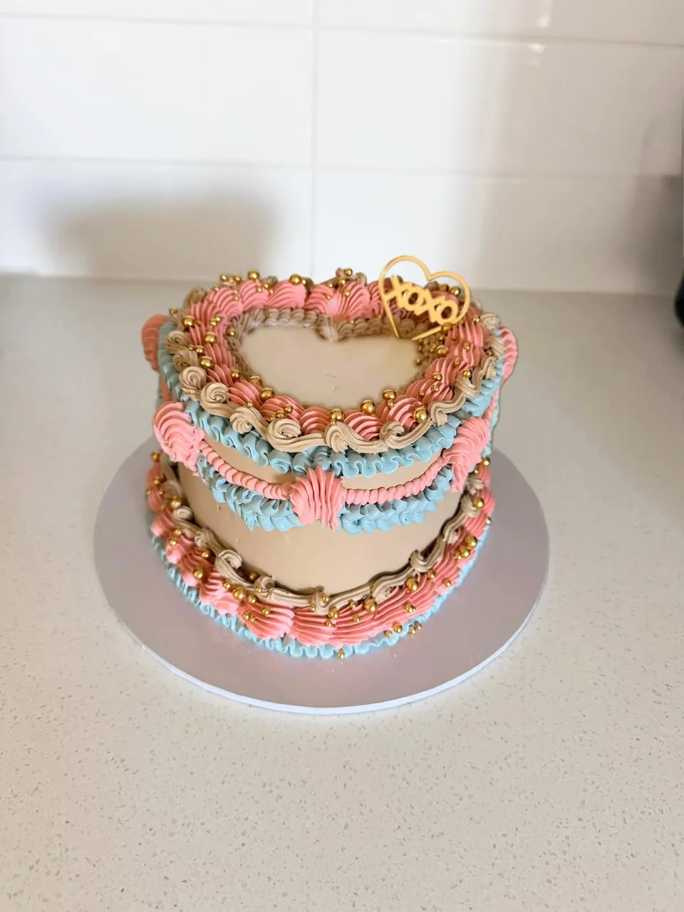 Beige vintage heart cake piped in pink and blue with gold pearls and a gold XOXO heart topper