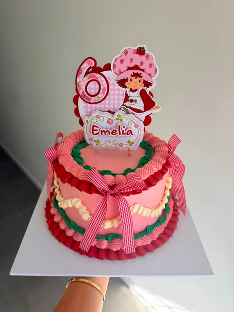 Pink vintage piped cake with red ruffles, green and cream piping, gingham bows and a Strawberry Shortcake topper for a sixth birthday